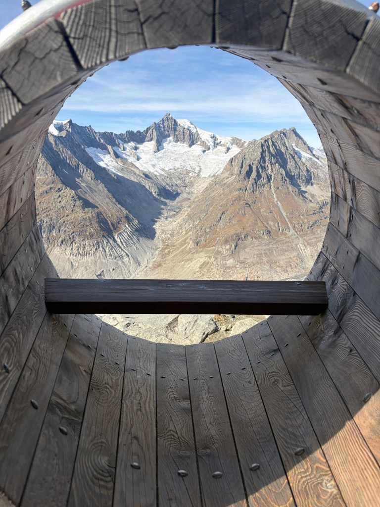 Mountain peaks seen through a circular wooden viewing frame near Bettmeralp.