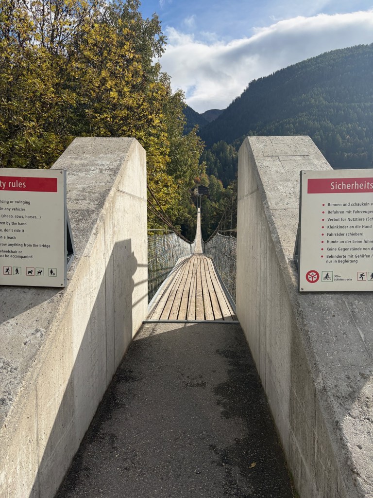 Suspension bridge stretching from concrete entrance pillars into an autumn valley.