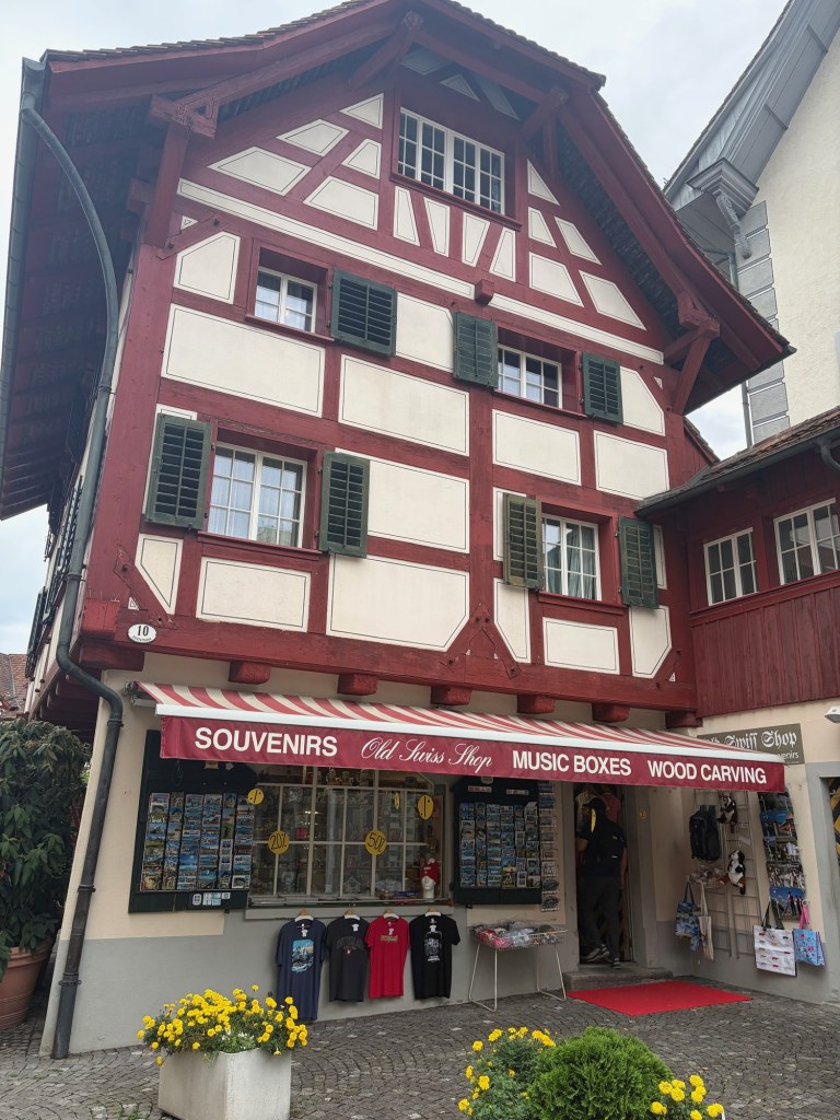 A red-and-white timbered building with green shutters, a souvenir shop, and yellow flowers.