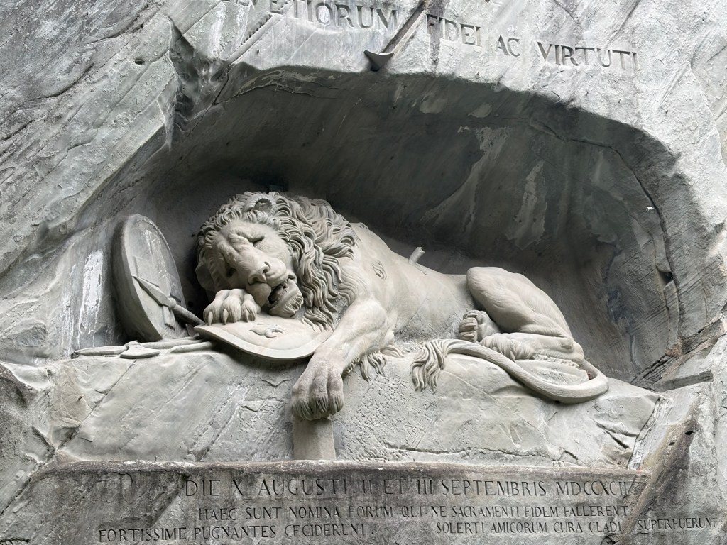 A reclining lion carved into a rock face rests its head on a shield.