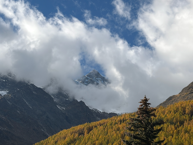 Clouds moving across a peak above golden forest