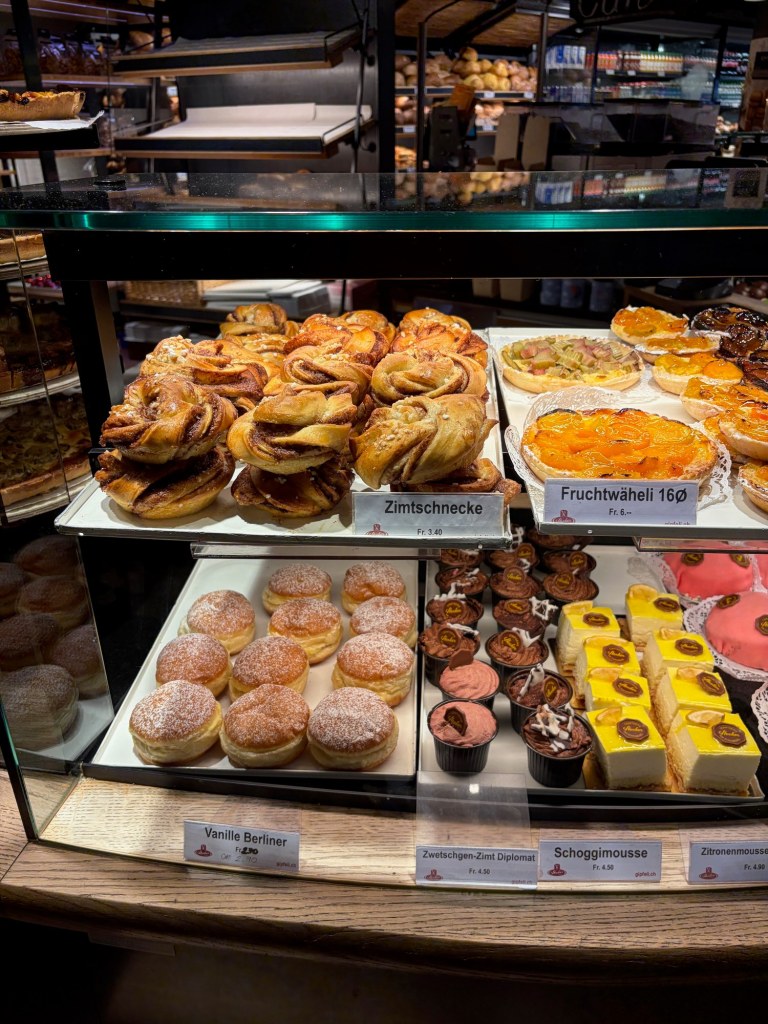 A bakery display filled with cinnamon pastries, fruit tarts, filled doughnuts, and small desserts.